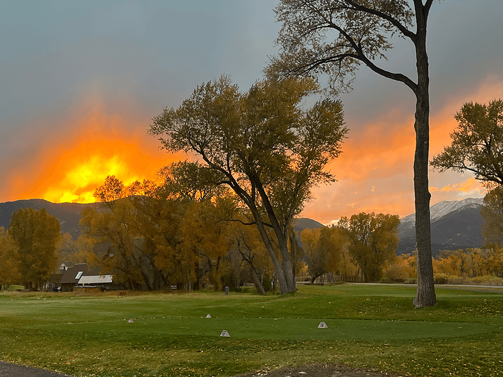 A picturesque sunset over a golf course surrounded by colorful autumn trees.