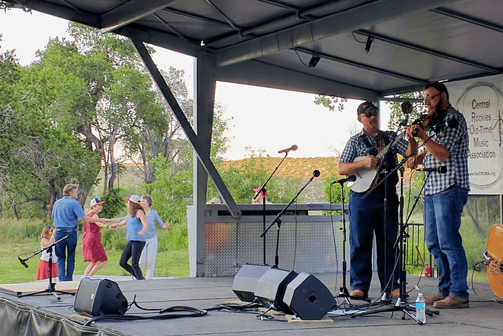 Musicians perform on stage while dancers enjoy the music outdoors.