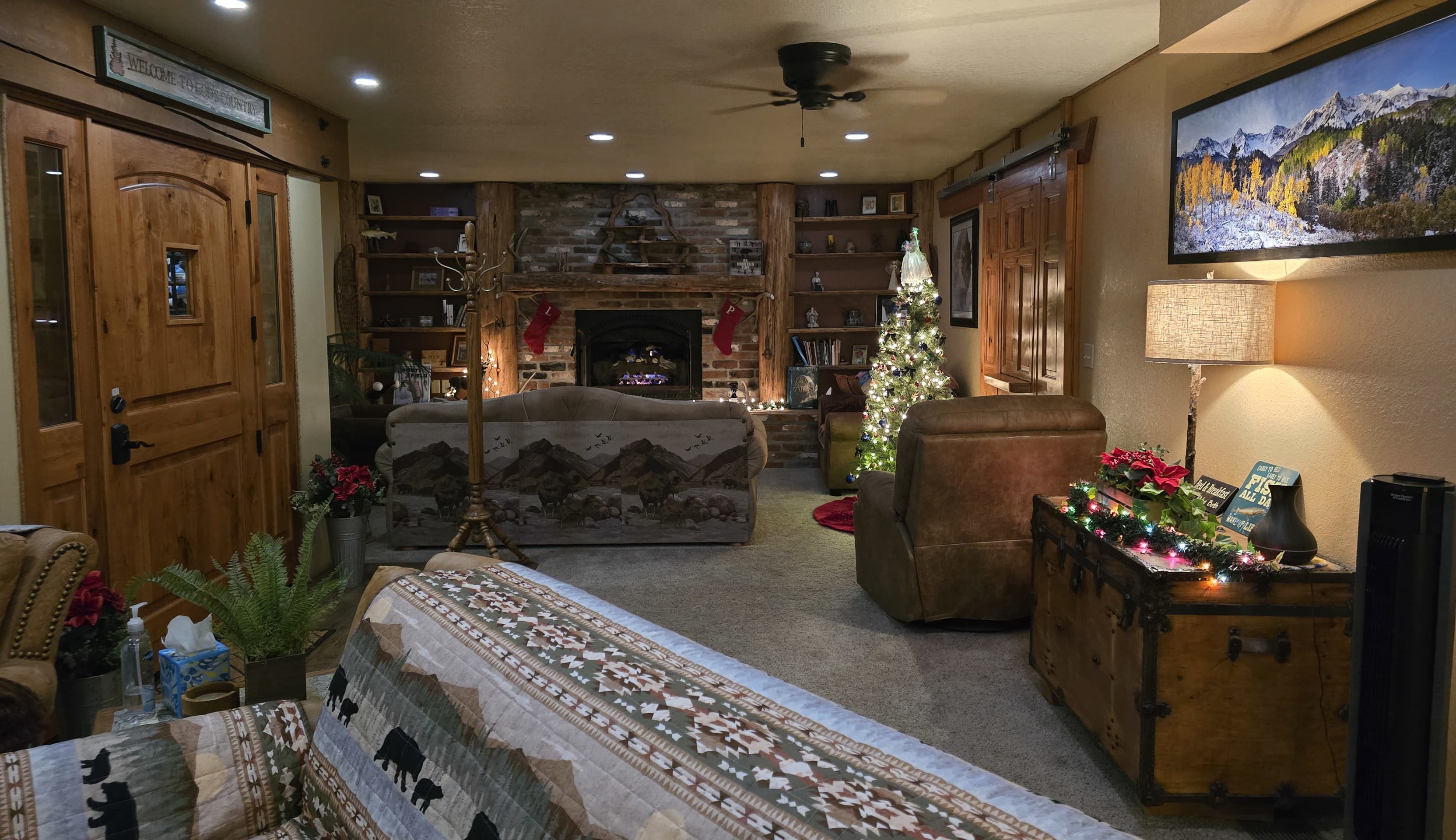 A cozy, warm living room featuring a stone fireplace, a decorated Christmas tree, and rustic wooden accents.
