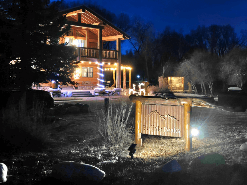 Illuminated log cabin with a "Buffalo Peaks" sign at night.