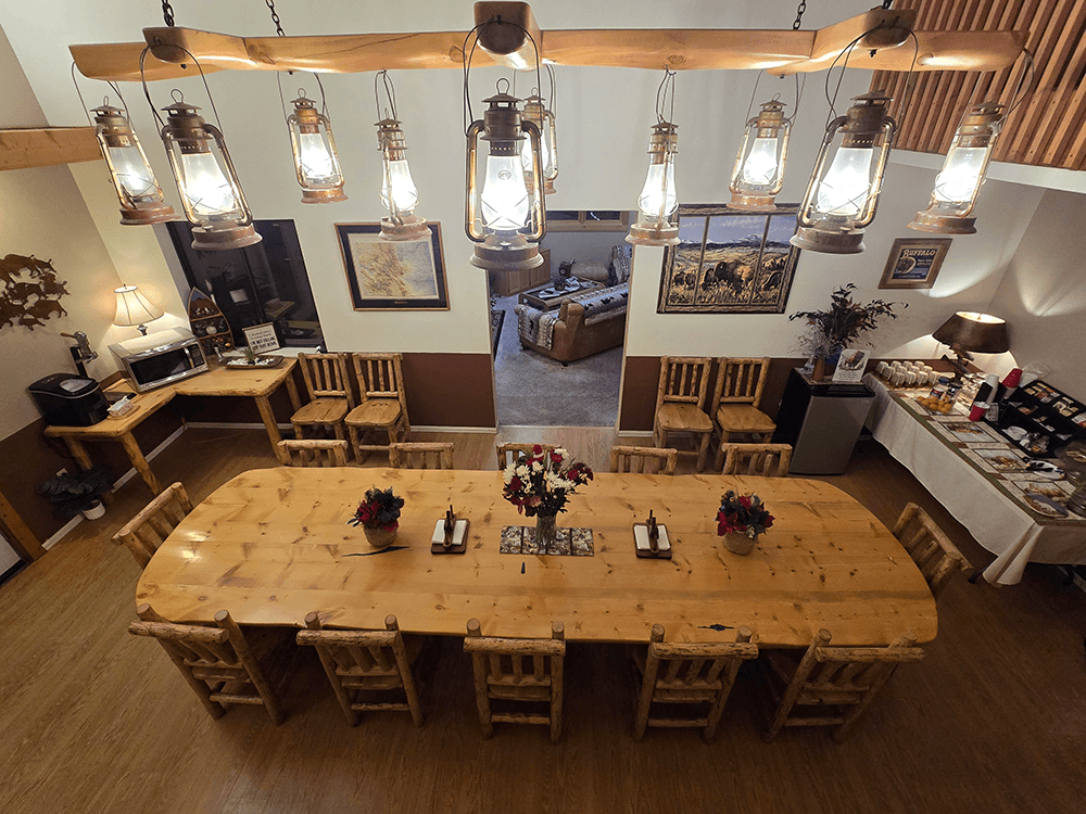 A large wooden dining table adorned with flowers and lanterns, set in a cozy rustic room with additional seating and soft lighting.