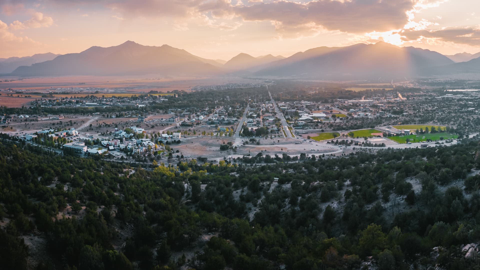 A panoramic view of a valley town surrounded by mountains at sunset.